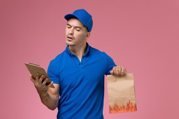 ピンクの壁にメモ帳食品パッケージを保持している青い制服の正面図男性宅配便、均一なサービスの仕事の配達