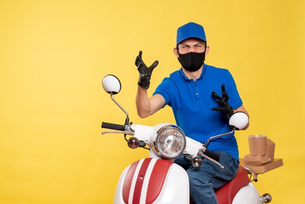 Вид спереди курьер-мужчина в синей форме и маске, сердитый на желтой работе covid- служба доставки пандемии, велосипед, вирус