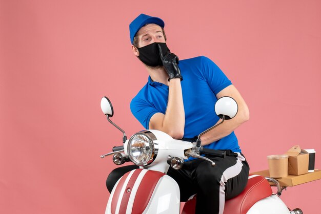 Front view male courier in blue uniform and mask on pink delivery virus fast-food service bike covid- job food