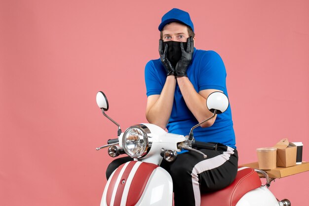 Front view male courier in blue uniform and mask on pink food fast-food service bike work covid- delivery job
