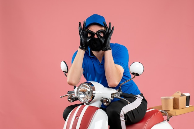 Front view male courier in blue uniform and mask on pink job delivery fast-food service bike covid- food virus
