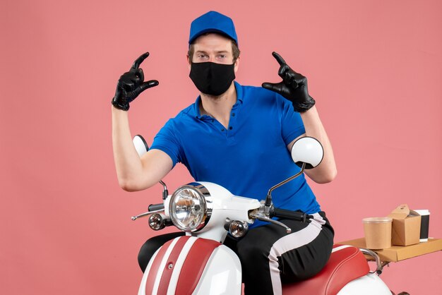 Front view male courier in blue uniform and mask on a pink job delivery fast-food service bike work covid- food virus