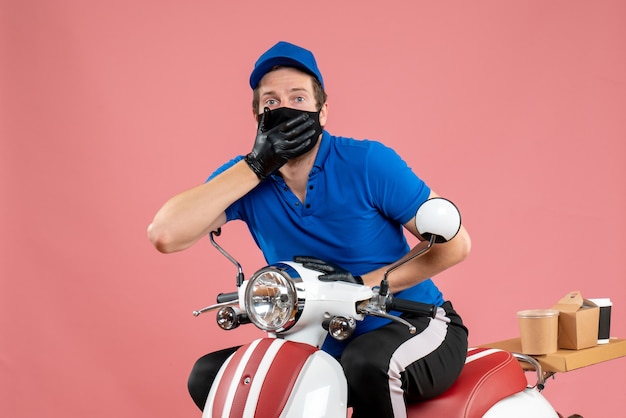 Front view male courier in blue uniform and mask on pink service fast-food covid- delivery job virus bike