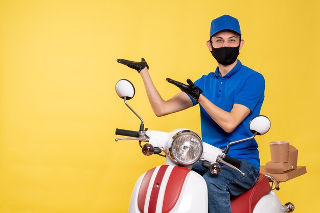Front view male courier in blue uniform and mask on yellow bike covid- pandemic service work delivery job virus