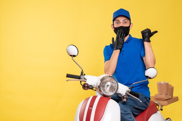 Front view male courier in blue uniform and mask on yellow work covid- delivery bike service job virus