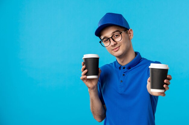 Front view of male courier in blue uniform with coffee on blue 