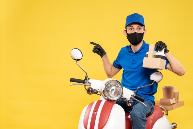 Front view male courier in blue uniform with coffee on a yellow pandemic bike covid- job delivery virus work service