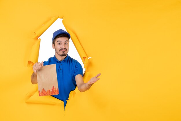 Курьер-мужчина, вид спереди в синей форме с продуктовым пакетом на желтом пространстве