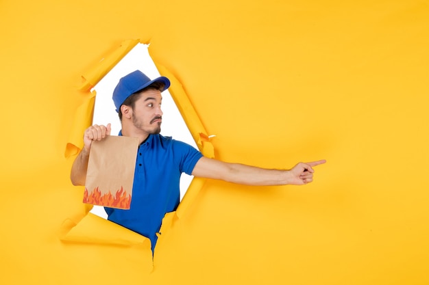 Free photo front view male courier in blue uniform with food package on a yellow space