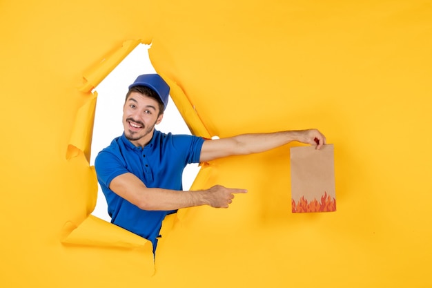 Front view male courier in blue uniform with food package on a yellow space