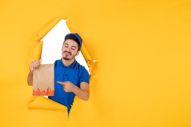 Front view male courier in blue uniform with food package on the yellow space