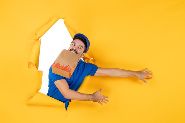 Front view male courier in blue uniform with food package on yellow space