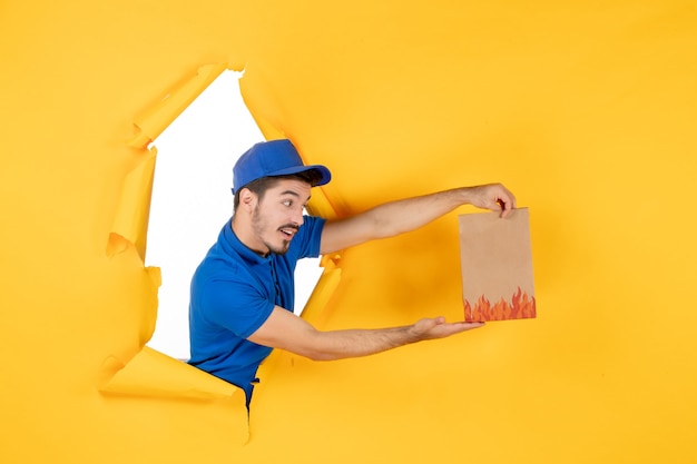 Front view male courier in blue uniform with food package on yellow space