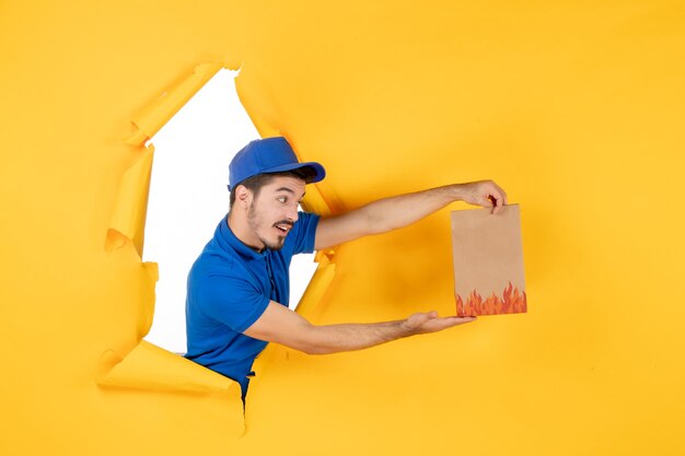Курьер-мужчина, вид спереди в синей форме с продуктовым пакетом на желтом пространстве