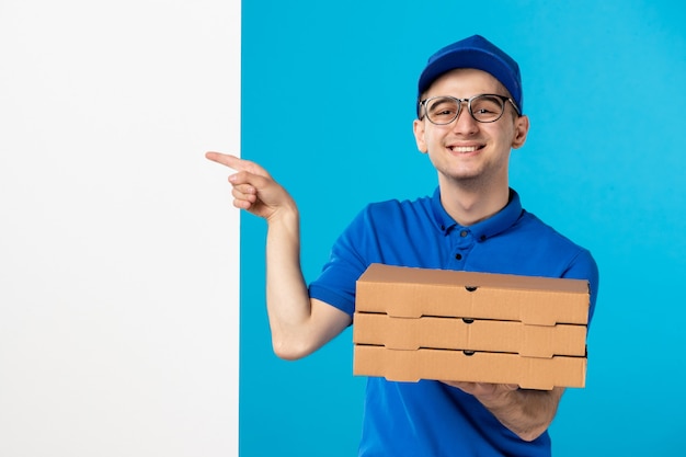 Front view of male courier in blue uniform with pizza on blue 
