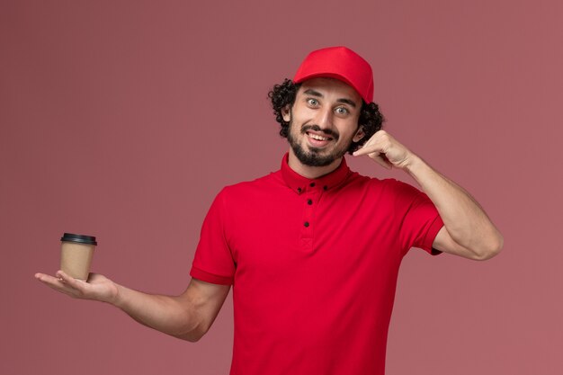 빨간 셔츠와 케이프 핑크 벽 서비스 유니폼 배달 직원 노동자에 갈색 커피 컵을 들고 전면보기 남성 택배 배달 남자