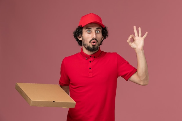 빨간 셔츠와 케이프 핑크 벽 서비스 배달 회사 직원 작업 작업에 배달 음식 상자를 들고 전면보기 남성 택배 배달 남자