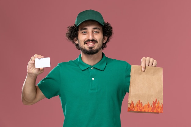 緑の制服とピンクの背景にカードと食品パッケージを保持しているケープの正面図男性宅配便制服配達男性の労働者の仕事