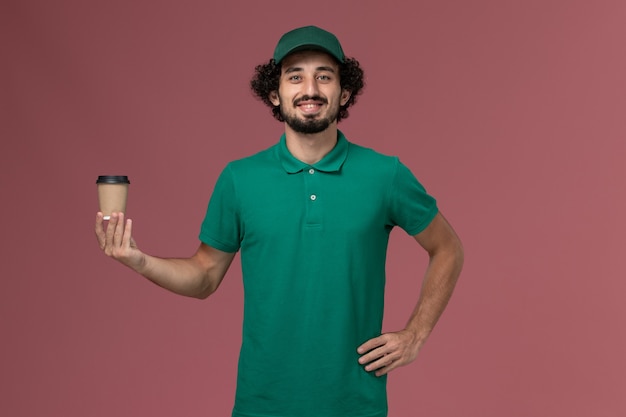 녹색 유니폼과 케이프 핑크 배경 유니폼 배달 서비스 작업에 배달 커피 컵을 들고 전면보기 남성 택배
