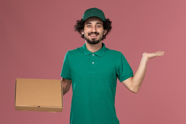 녹색 유니폼과 케이프 음식 상자를 들고 분홍색 배경에 웃는 전면보기 남성 택배 서비스 작업자 작업 유니폼 배달