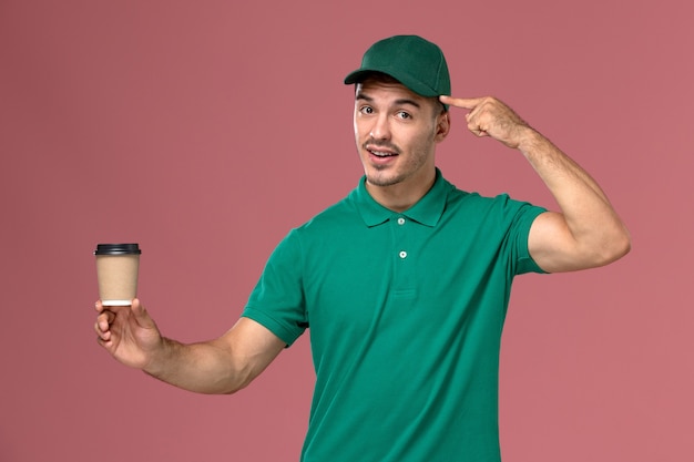 밝은 분홍색 배경에 배달 커피 컵을 들고 녹색 제복을 입은 전면보기 남성 택배