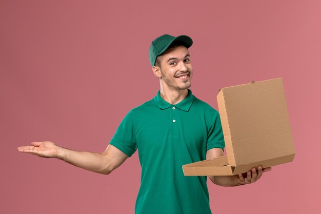 녹색 유니폼을 들고 밝은 분홍색 배경에 음식 상자를 여는 전면보기 남성 택배