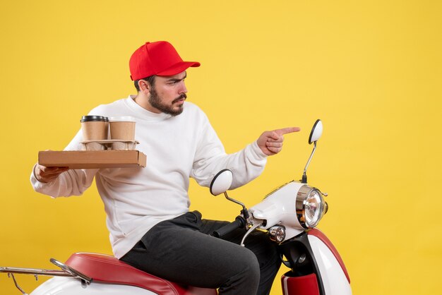 Front view of male courier holding delivery coffee and food on the yellow wall