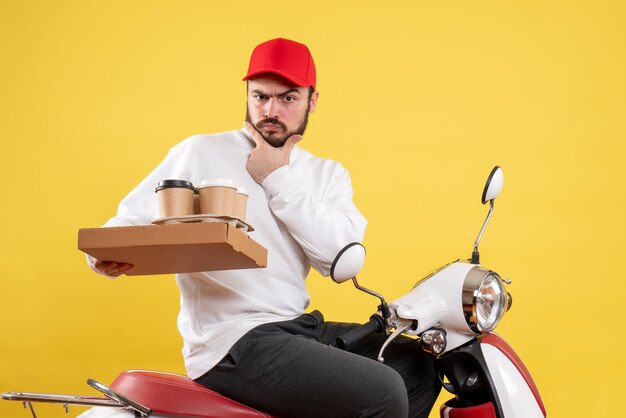 Front view of male courier holding delivery coffee and food on yellow wall