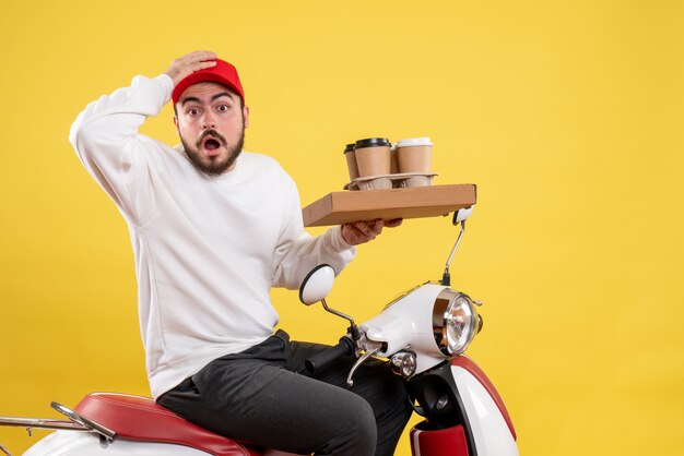 Front view of male courier holding delivery coffee and food on yellow wall