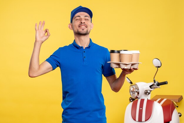 Front view male courier holding delivery coffee on the yellow color worker service work delivery uniform bike job