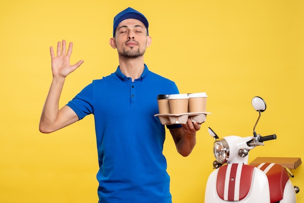 Corriere maschio di vista frontale che tiene il caffè di consegna sul lavoro uniforme della bici del lavoro di servizio dell'operaio di colore giallo