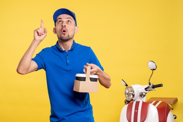 Corriere maschio di vista frontale che tiene il caffè di consegna sul lavoro uniforme della bici di servizio di lavoro di lavoro di colore giallo dell'operaio