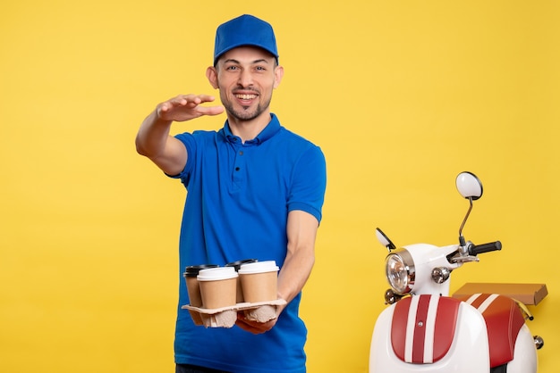 Corriere maschio di vista frontale che tiene il caffè di consegna sulla bici uniforme di emozione di servizio di colori gialli