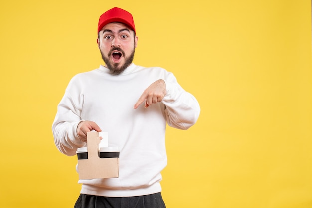 Front view of male courier holding delivery coffee on a yellow wall