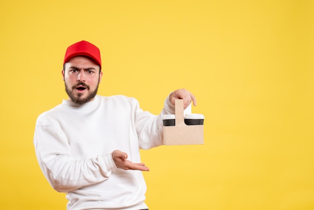 Free photo front view of male courier holding delivery coffee on the yellow wall