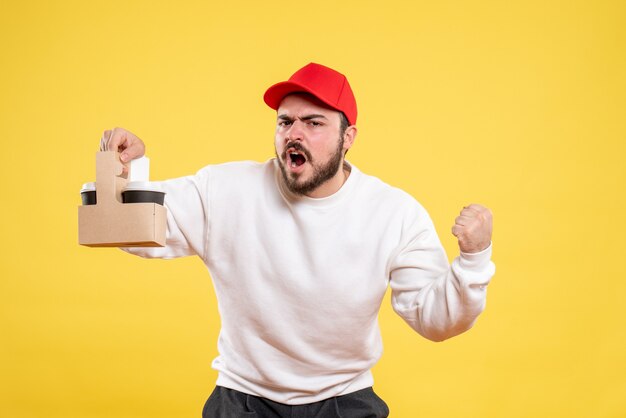 Front view of male courier holding delivery coffee on the yellow wall