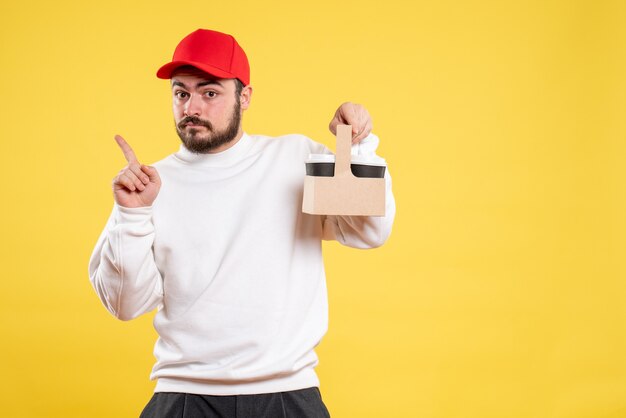 Front view of male courier holding delivery coffee on yellow wall