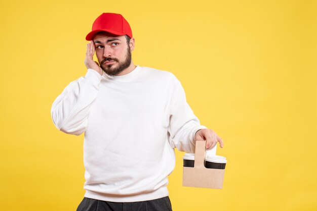 Front view of male courier holding delivery coffee on yellow wall