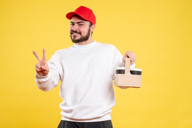 Front view of male courier holding delivery coffee on yellow wall