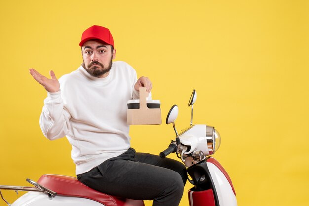 Front view of male courier holding delivery coffee on yellow wall