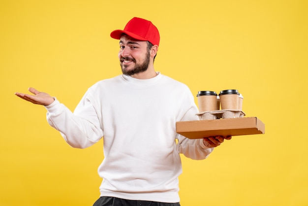 Front view of male courier holding delivery food and coffee on yellow wall