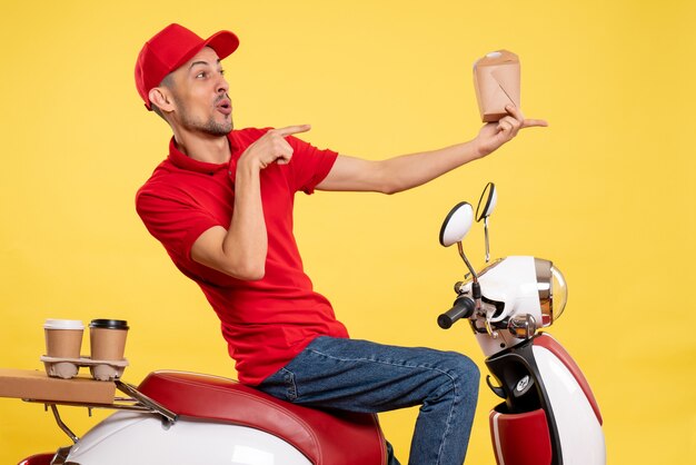 Corriere maschio di vista frontale che tiene poco cibo di consegna sui colori dell'alimento di servizio uniforme del lavoro di consegna della bici dell'operaio giallo