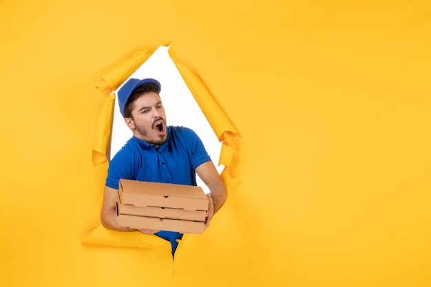 Foto gratuita corriere maschio vista frontale che tiene scatole per pizza su spazio giallo