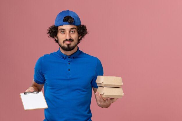 無料写真 青いユニフォームとピンクの壁にメモ帳付きの配達食品パッケージを保持しているケープの正面図男性宅配便制服配達サービス作業