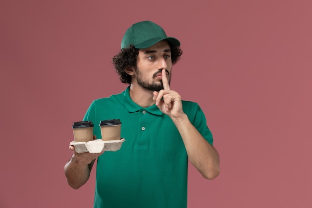 無料写真 緑の制服とピンクの背景に配達コーヒーカップを保持しているケープの正面図男性宅配便サービス制服配達仕事男性の仕事