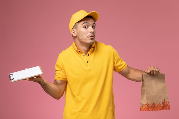 ピンクの背景にメモ帳と食品パッケージを保持している黄色の制服を着た正面男性宅配便