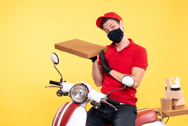 Front view male courier in mask holding food box on yellow 