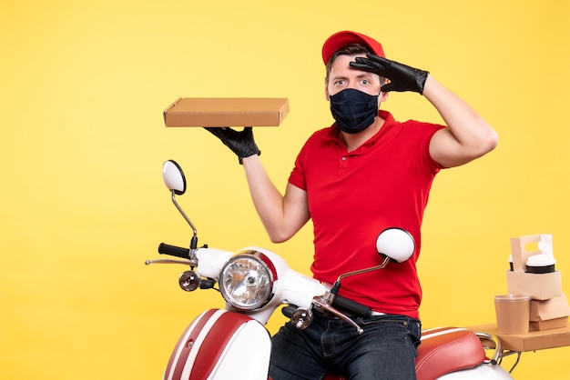 Free photo front view male courier in mask holding food box on yellow