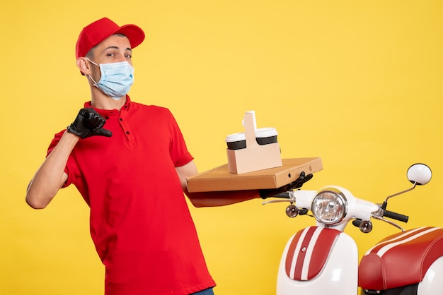 Вид спереди мужчина-курьер в маске с доставкой кофе и коробкой на желтой службе covid pandemic color рабочая форма