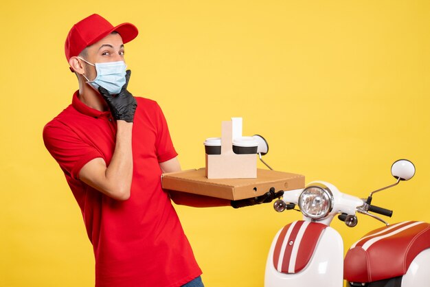 Front view male courier in mask with delivery coffee and box on the yellow service covid pandemic color virus job work uniform